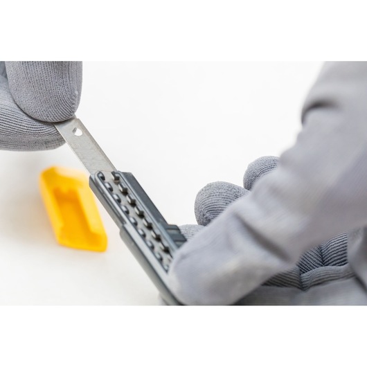 STANLEY 0-10-150 utility knife blade held in gloved hands close-up, yellow blade cover in background.
