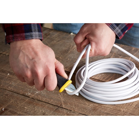 STANLEY 0-10-234 utility knife cutting white cable, close-up view on wooden surface.