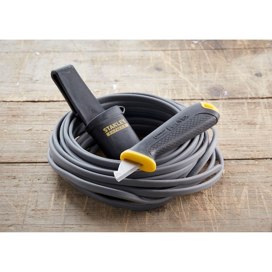 Photo of STANLEY 0-10-234 utility knife with black sheath on coiled gray cable, placed on wooden surface.