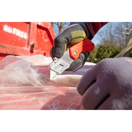 Photo of STANLEY 0-10-243 utility knife cutting plastic sheet outdoors, worker wearing gloves.