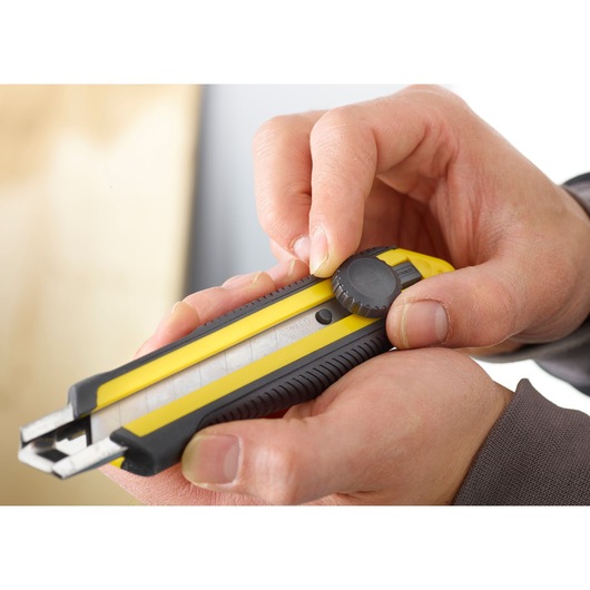 Photo of STANLEY 0-10-417 utility knife with yellow and black body, shown in hand, adjusting blade with knob.