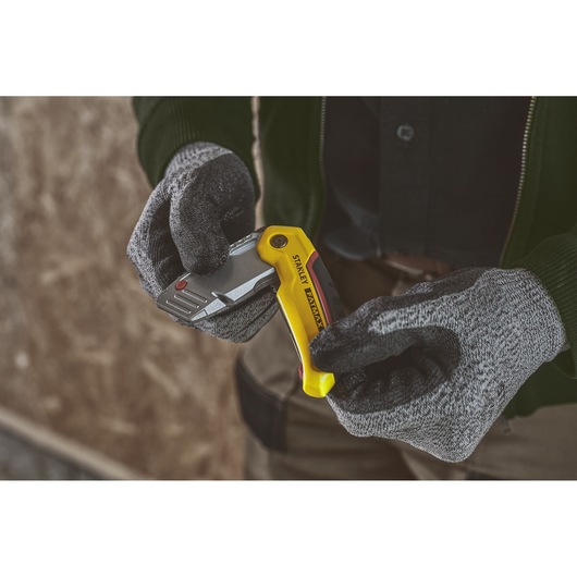 Photo of STANLEY 0-10-825 folding utility knife with yellow handle held by gloved hands, indoor setting.