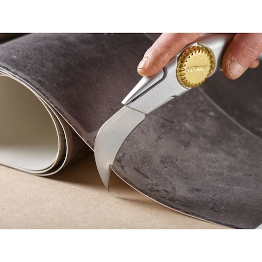 STANLEY 0-11-980 photography of carpet cutter with gold wheel cutting dark carpet material.