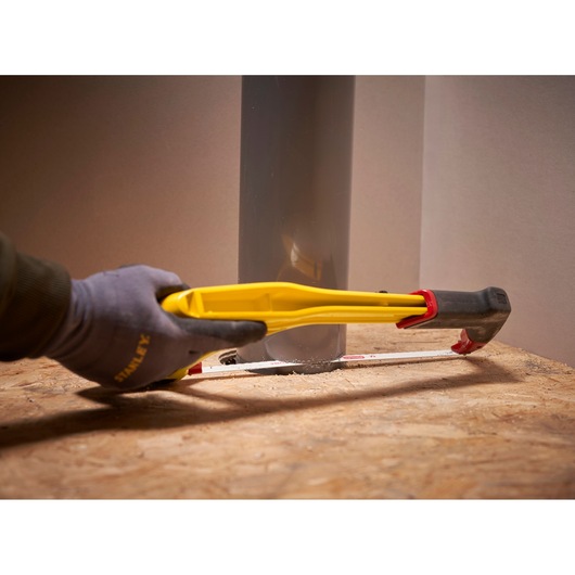 Photo of STANLEY 0-20-108 yellow hand saw cutting wood near a grey pipe, held by a gloved hand.