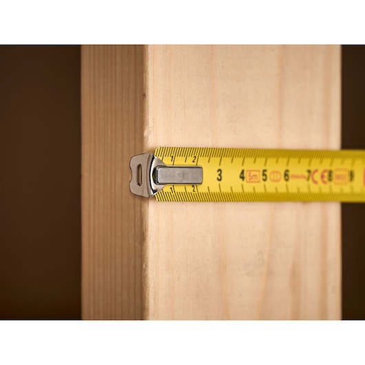 STANLEY 0-33-194 tape measure in use, measuring wooden plank, close-up side angle.