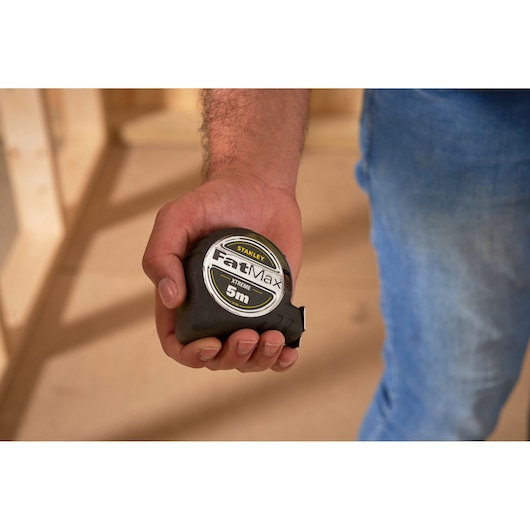 Photo of a hand holding a STANLEY 0-33-887 FatMax XTREME 5m tape measure, indoor setting.