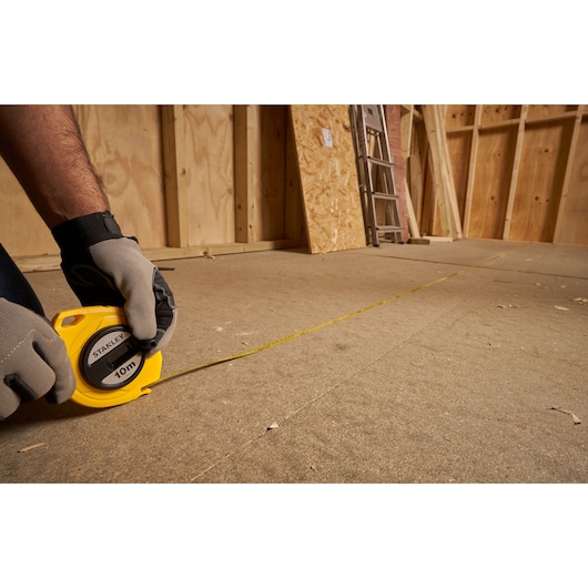 Photo of STANLEY 0-34-102 tape measure being used on a construction floor, yellow casing visible.