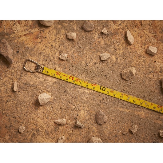 STANLEY 0-34-102 yellow tape measure on a dusty surface with scattered stones, top view.