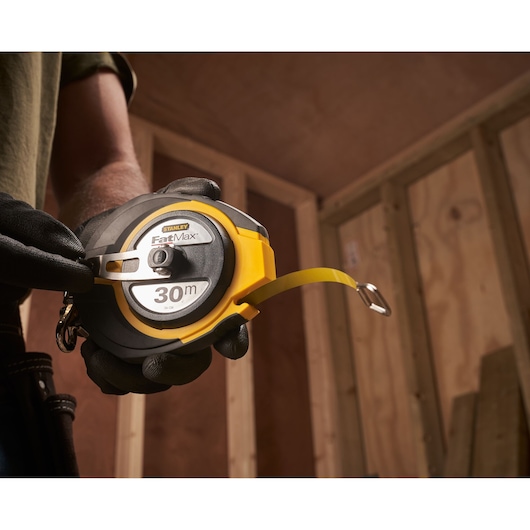 STANLEY 0-34-134 FatMax 30m tape measure held in gloved hand at a construction site.