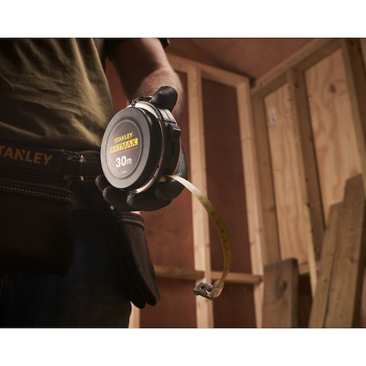 Photo of STANLEY 0-34-203 measuring tape, 30m, held by a person in a workshop.