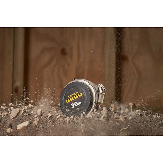 STANLEY 0-34-203 tape measure, 30m FATMAX, rugged design shown in action with dirt and rocks in the foreground.