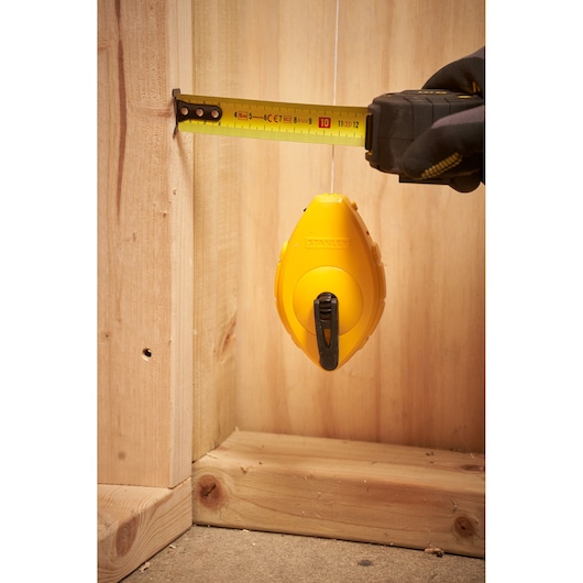 STANLEY 0-47-440 chalk line reel in use with measuring tape near wooden framing, close-up.