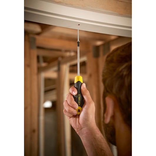 Photo of STANLEY 0-64-974 screwdriver with black and yellow handle in use tightening a screw overhead.