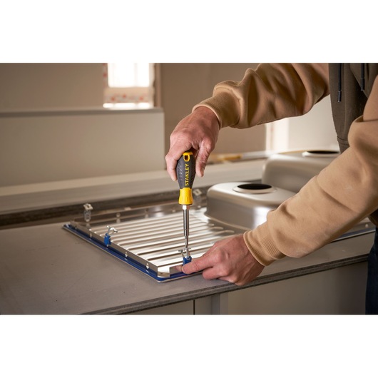 STANLEY 0-68-012 screwdriver used to install a metal sink in a kitchen, close-up from side.