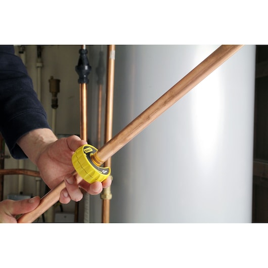 STANLEY 0-70-446 pipe cutter in use on a copper pipe, yellow tool held by hand in plumbing setting.
