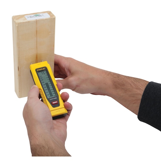 STANLEY 0-77-030 moisture meter held against wood, close-up on white background.