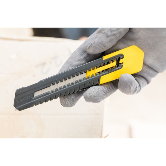STANLEY 1-10-151 snap-off utility knife, black and yellow, held in gloved hand, close-up photography.