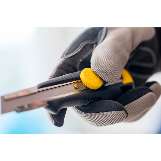 STANLEY 1-10-418 utility knife with yellow knob held in gloved hand, close-up photo.