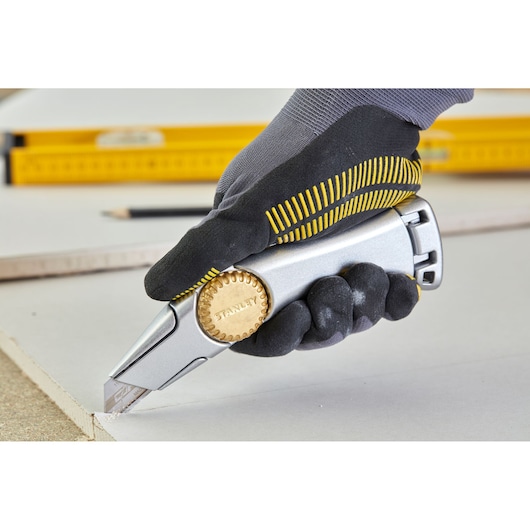 STANLEY 1-10-550 utility knife with gold wheel, gloved hand cutting drywall, in use.