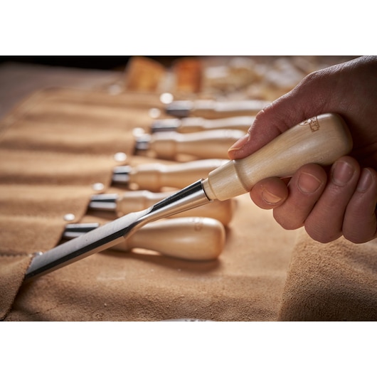 STANLEY 1-16-793 wood chisel held in hand, with chisels in tan suede roll on table, close-up.