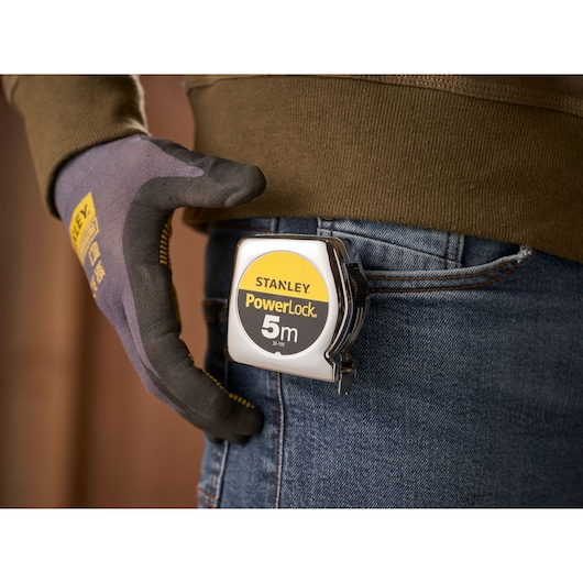 STANLEY 1-33-191 tape measure clipped to jeans pocket, person wearing gloves.