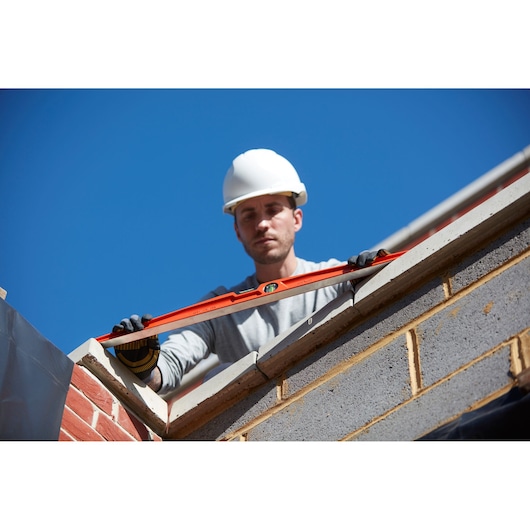 STANLEY 1-42-315 spirit level held by gloved worker on brick wall, outdoor construction scene.