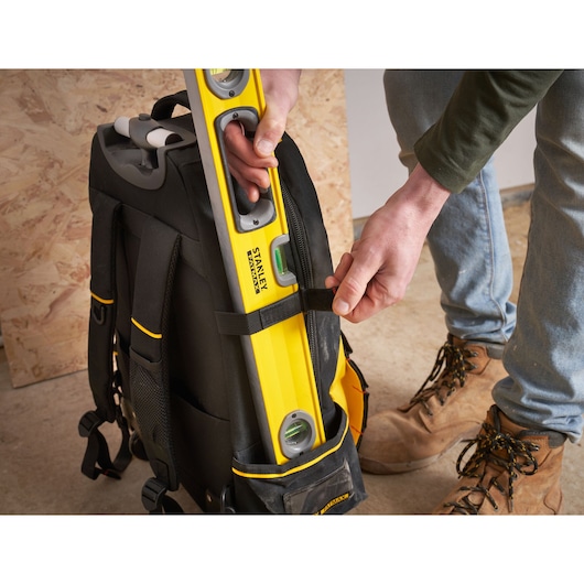 STANLEY 1-79-215 black tool backpack with yellow level stored in side pocket, close-up, indoor setting.