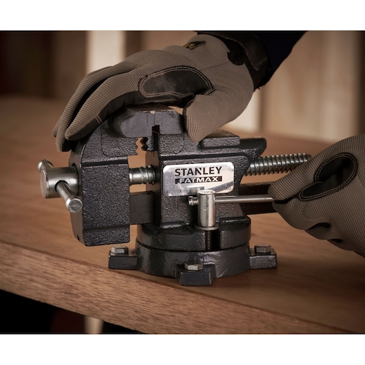 Photo of STANLEY 1-83-065 bench vise mounted on a workbench, operated by gloved hands.