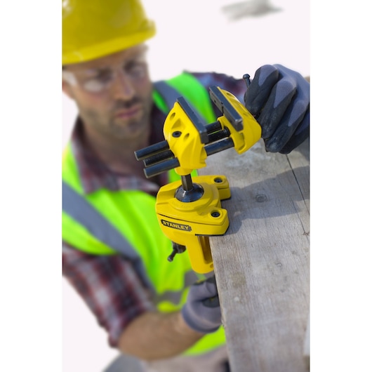 STANLEY 1-83-069 bench vise clamped to wood, side angle, yellow tool, worker in safety gear visible.