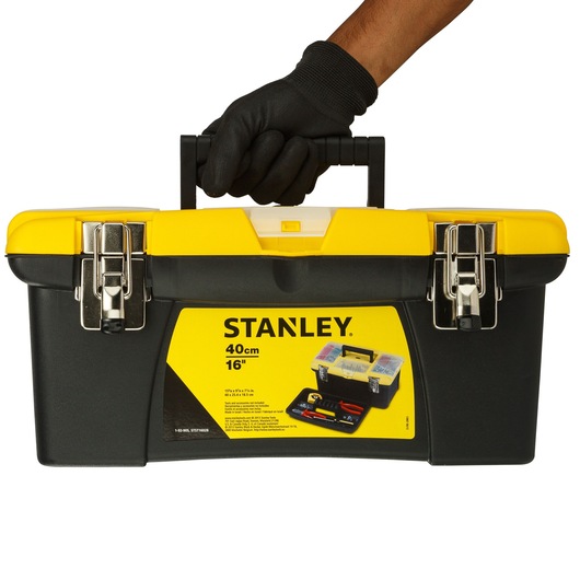 Stanley 1-92-905 tool box, black and yellow, front angle, held by gloved hand, metal latches, plastic handle.