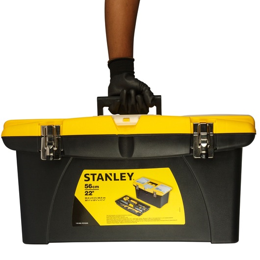 Stanley 1-92-908 tool box, yellow and black, front angle, held by gloved hand, white background.