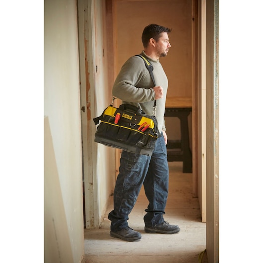Worker carrying STANLEY 1-93-950 tool bag with shoulder strap, filled with hand tools, in an indoor construction setting.