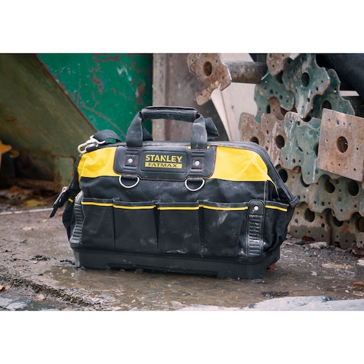 STANLEY 1-93-950 tool bag with yellow and black fabric, multiple pockets, handles, shown outdoors on wet ground.