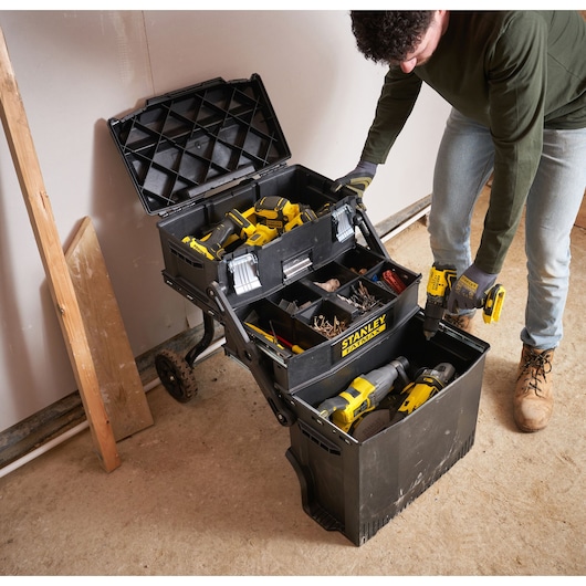 STANLEY 1-94-210 mobile tool chest with open lid showing organized power tools, fasteners, and accessories on a worksite.