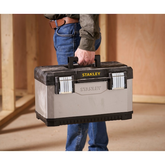 Stanley 1-95-615 toolbox with black lid and silver body, carried by person indoors.