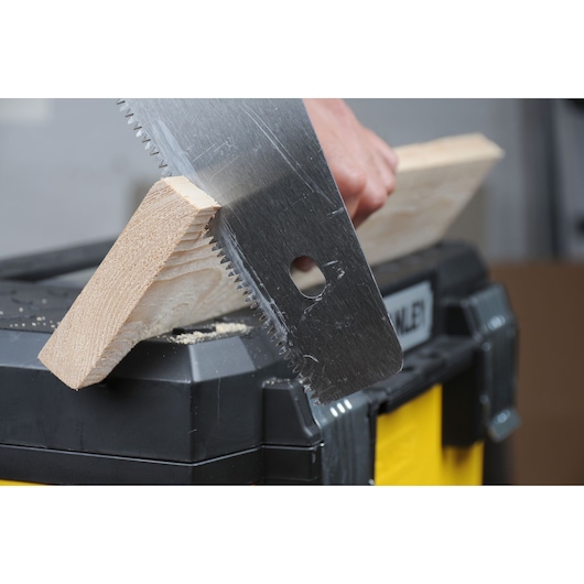 STANLEY 1-95-621 saw cutting wood plank on black and yellow toolbox, close-up photography.