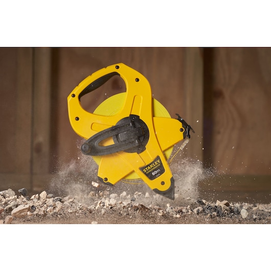 STANLEY 2-34-775 open reel yellow measuring tape, 60m length, handheld with black handle, on construction debris.
