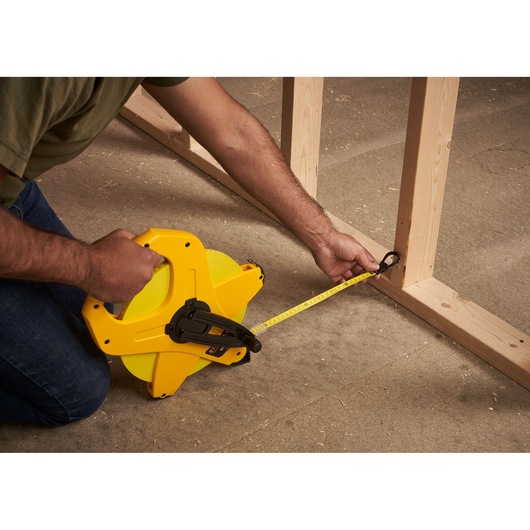 STANLEY 2-34-777 tape measure in use measuring wood framing, side angle, yellow casing.