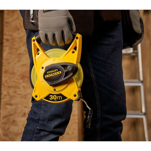 STANLEY 2-34-814 open reel 30m FATMAX tape measure held by a gloved hand, workshop background.