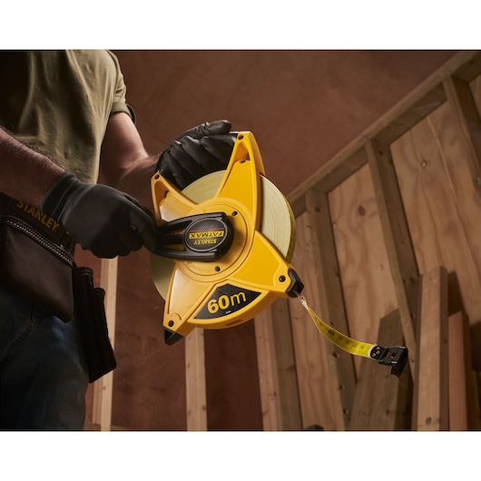 Stanley 2-34-824 yellow 60m tape measure held by gloved hand at construction site.