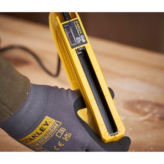 STANLEY 6-TRE550 electric stapler close-up held in gloved hand, yellow body, wood surface underneath.