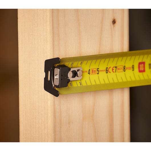 STANLEY FMHT0-33868 tape measure with yellow blade measuring wooden plank, close-up side view.