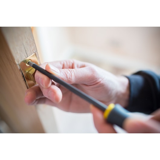 STANLEY FMHT0-62064 screwdriver photography of hand tightening screw on brass door latch.