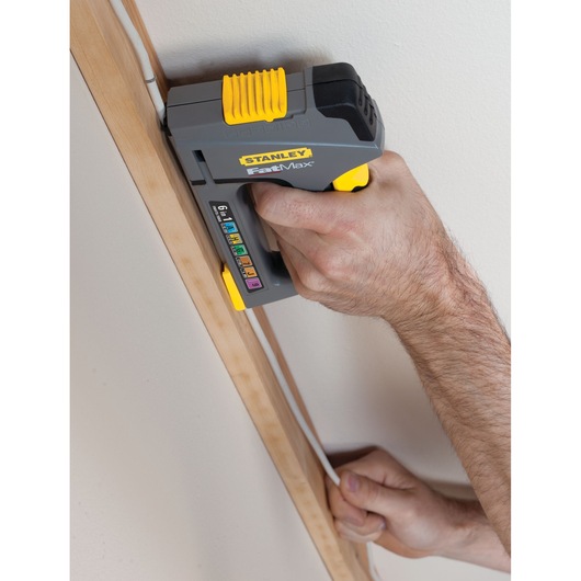 STANLEY FMHT0-70868 stapler fastening cable to wall trim, close-up photo of hand-held tool.
