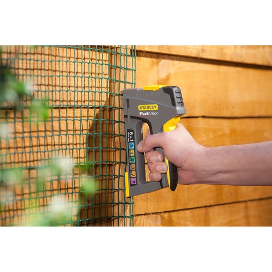Stanley FMHT0-70868 FatMax staple gun held against green mesh on wooden fence, side view.