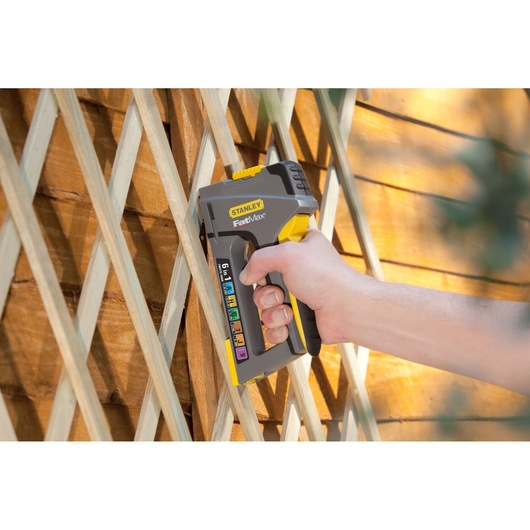 STANLEY FMHT0-70868 stapler held against wooden lattice, yellow and grey, product in use.