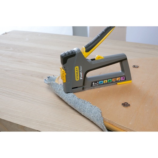 STANLEY FMHT0-70868 staple gun, grey and yellow, fastening fabric to wood, side angle, photography.