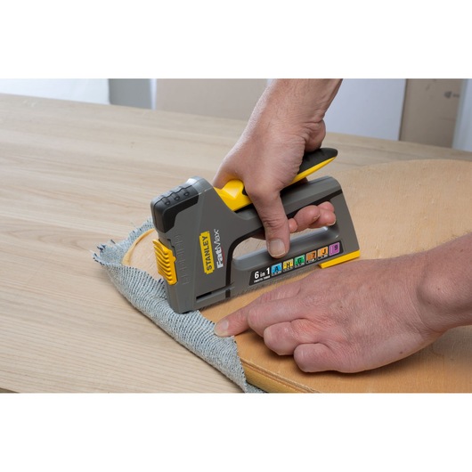 STANLEY FMHT0-70868 hand stapler fastening fabric to wood, side angle, photo of product in use.
