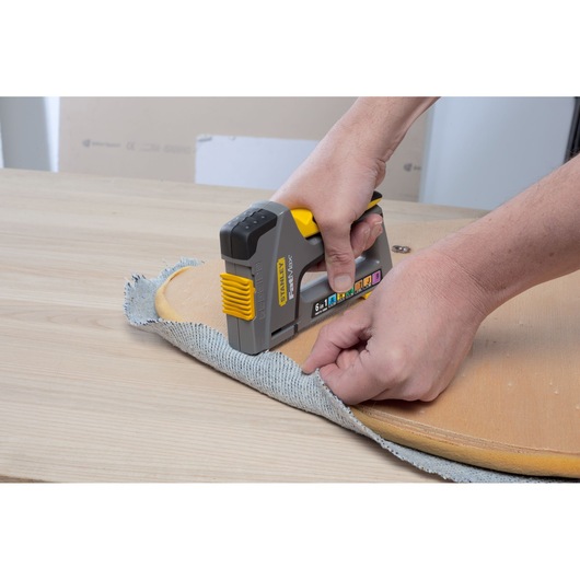 Photo of STANLEY FMHT0-70868 stapler fastening fabric to wood, product in use, close-up angle.