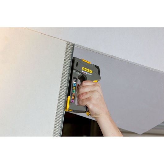STANLEY FMHT0-70868 staple gun in use attaching mesh to drywall, close-up view.